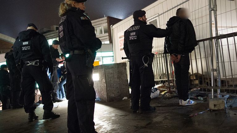 Kolme poliisia ja pidätetty, jolla on käsiraudat. 