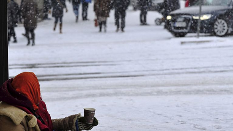 Nainen kerjäämässä kadulla lumisateessa.