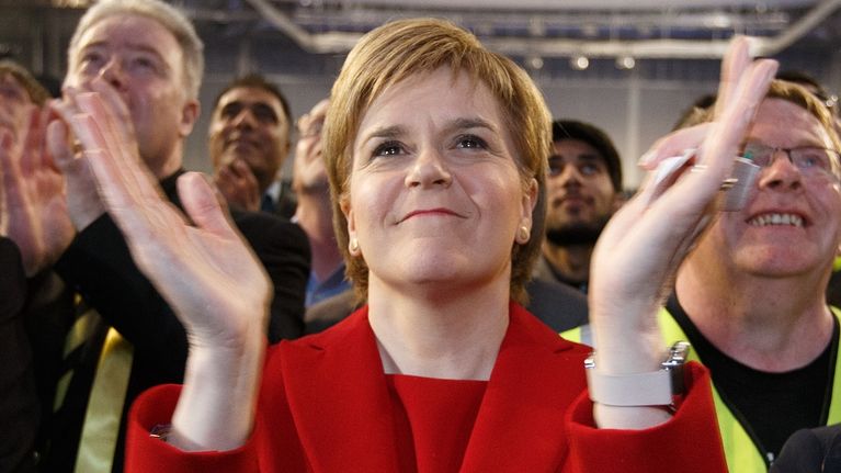 Hymyilevä Sturgeon taputtaa käsiään puoluetoverien ympäröimänä. 