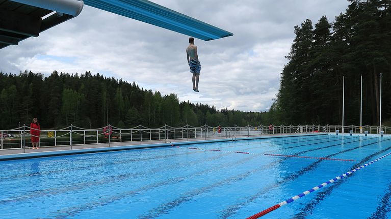 Mies hyppää hyppytornista altaaseen maauimalassa