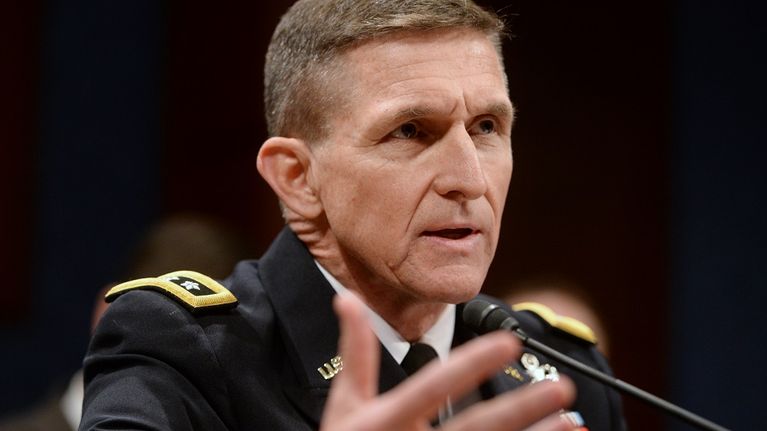Flynn puhuu mikrofoniin vahvistaen sanojaan oikealla kädellään. Hänellä on yllään tumma univormu, jonka kauluksessa on kultaisin kirjaimin U.S. Rintamuksessa on sarja ansiomerkkejä. Kuvan tausta on musta.