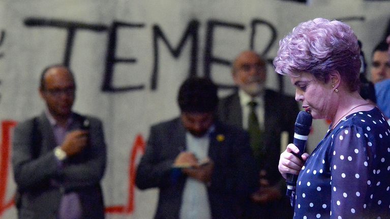 Seinässä teksti Temer, etualalla mikrofoniin puhuva Dilma Rousseff.