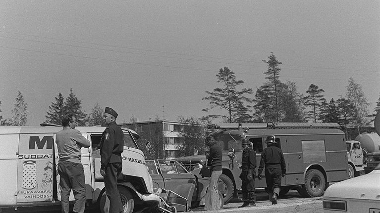 Liikenneonnettomuus moottoritiellä Helsingissä vuonna 1970. Paloauto ja muita autoja kolarissa, poliisi, palomiehiä ja ihmisiä onnettomuuspaikalla. 