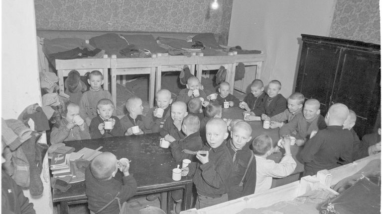 Noin kaksikymmentä poikalasta syömässä ahtaassa tilassa jossa on kerrossänkyjä.