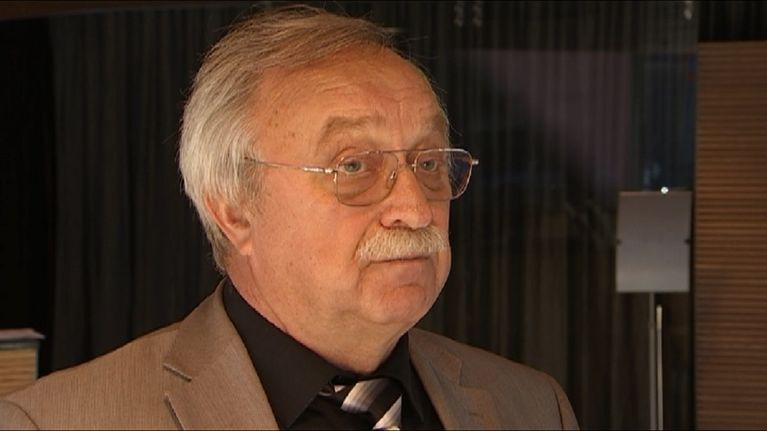 Oleg Bodrov kuvattuna Eduskunnan kansalaisinfon tiloissa. Hänellä on silmälasit, harmaa tukka ja viikset. Yllään Bodrovilla on ruskea irtotakki, musta kauluspaita ja valko-mustaraitainen kravatti.