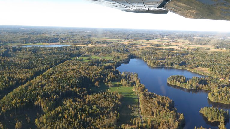 Järvi- ja metsämaisemaa ilmasta kuvattuna, ylälaidassa lentokoneen siipi.