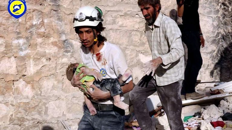 Avustustyöntekijä kuljettaa lasta turvaan Aleppossa.