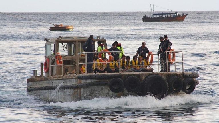 Australian maahanmuuttoviranomaiset kuljettavat pakolaisia veneen kannella.