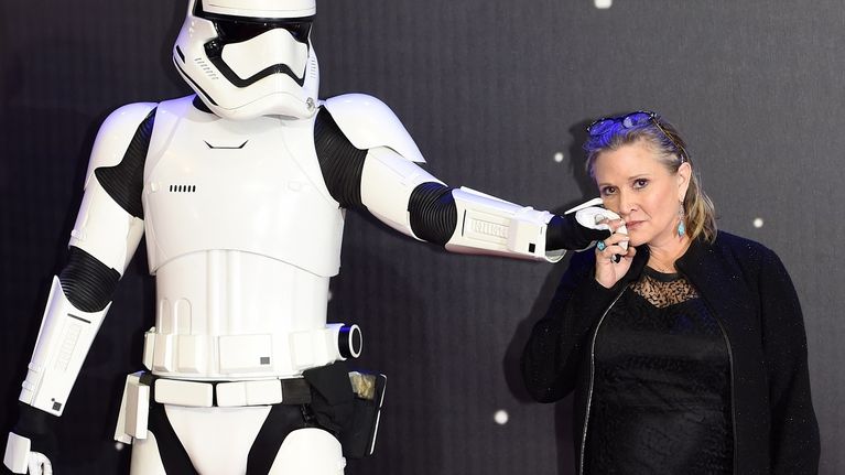 Mustaan pukeunut nainen pitää valkoisen Stormtrooper elokuvahahmon kättä poskellaan. 