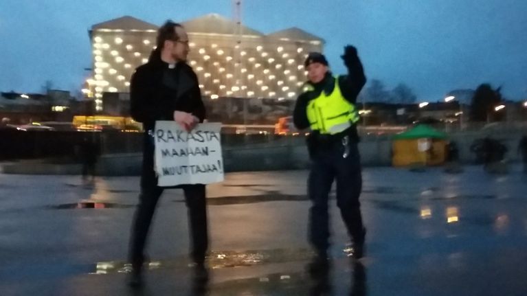 Poliisi poistaa Pastori Kai Sadinmaan Helsingin Kansasaistorilta itsenäisyyspäivänä 2015. Syynä Sadinmaan Rajat Kiinni -mielenosoitusta vastaan järjestämä yhden miehen vastamielenosoitus.