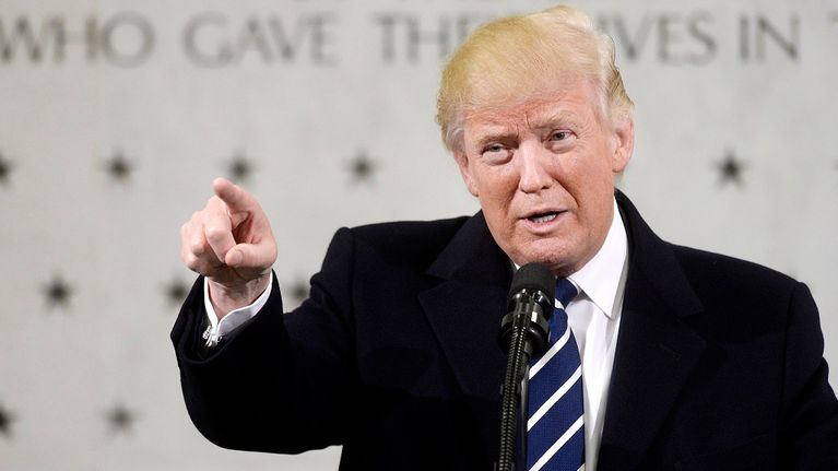 Trump puhuu osoittaen kuulijoita oikean kätensä etusormella. Taustalla näkyy CIA:n päämajan seinää, jossa muistetaan tähdillä palveluksessa kuolleita CIA:n työntekijöitä.