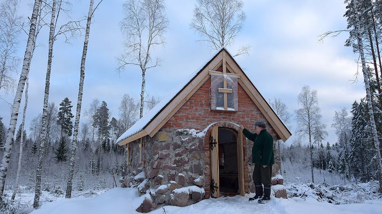 Mies rakentamansa pienen kivikirkon ulko-ovella talvella