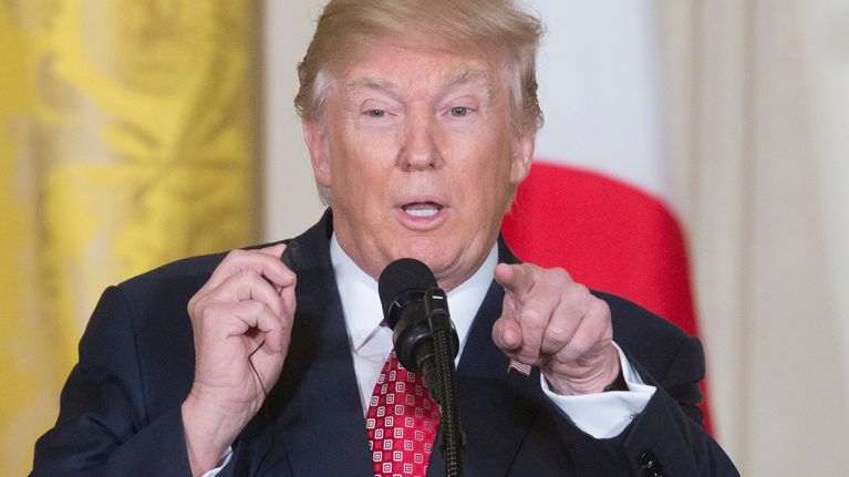 Donald Trump mikrofonin takana, osoittaa sormelle eteenpäin. 