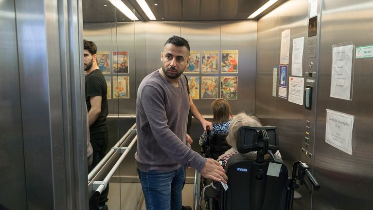Osama hississä työkaverinsa pyörätuolissa istuvien rouvien kanssa.