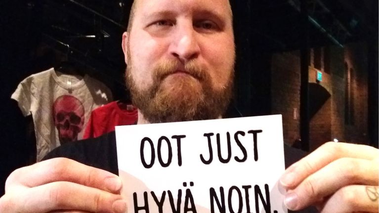 Rap-artisti Paleface esittelee Oot just hyvä noin -kampanjan pientä julistetta.