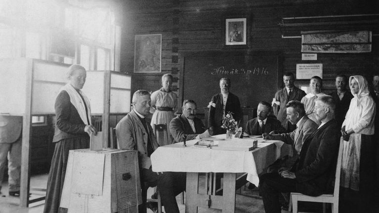 Vaalitoimitsijoita. Äänestäjä pudottaa äänestyslippuaan vaaliuurnaan Hauhon koululla eduskuntavaaleissa 1916.
