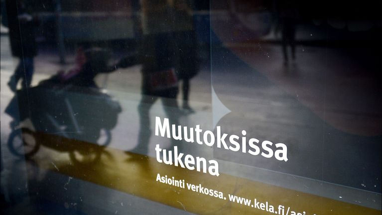 Nainen ja lastenvaunut heijastuvat Kansaneläkelaitoksen toimipisteen ikkunasta.