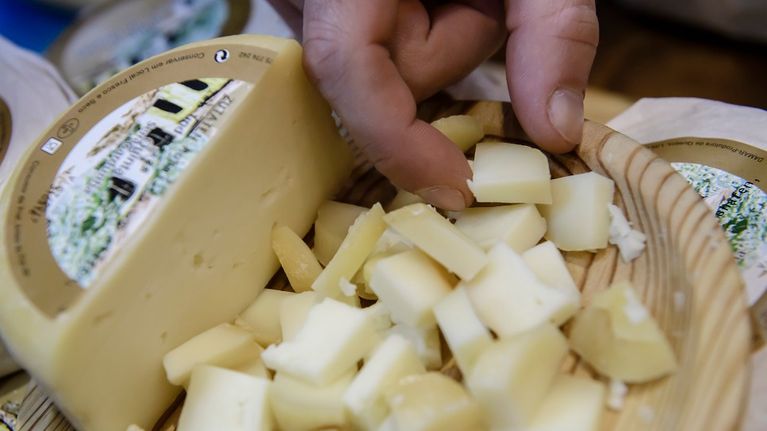 Miehen käsi poimii juustonpalaa vadilta, johon on kuutioitu puolikas juustokiekosta. 