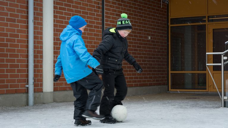 Kaksi koululaista pelaa jalkapalloa välitunnilla.