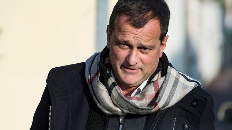 Louis Aliot kävelee mustassa päällystakissa, kaulaliina huolettomasti kietaistuna kohti kameraa.