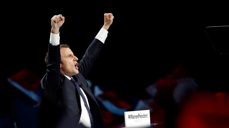 Tummaan pukuun pukeutunut Macron tuulettaa nyrkit ilmassa.
