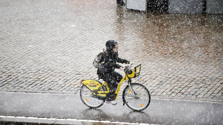 Nainen pyöräilee kaupunkipyörällä lumisateessa Helsingissä.