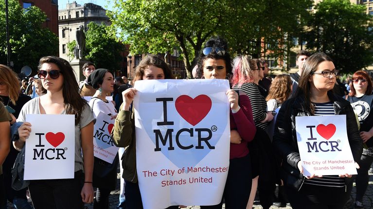 Joukko ihmisiä. Eturivissä olevilla on julisteet, joissa lukee I love MCR, The City of Manchester Stands United.