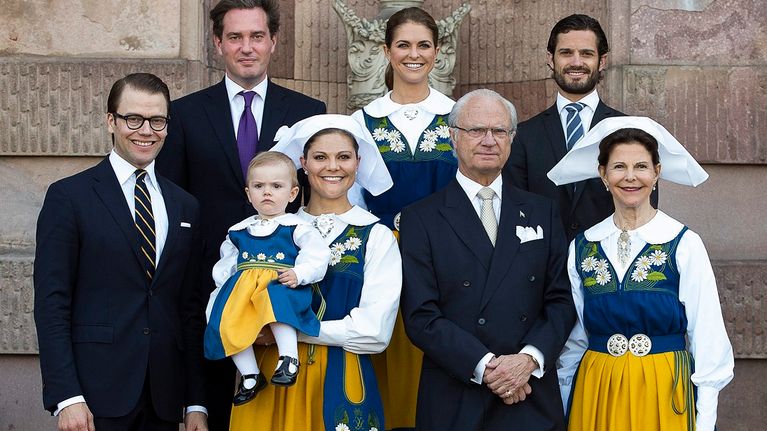 Kuningasperheen naiset ja pikkuprinsessa kansallispuvuissa, miehet tummissa puvuissa. 