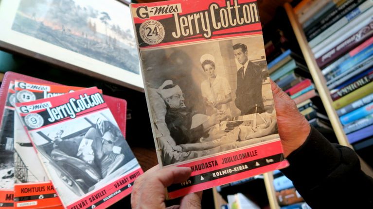 Jerry Cottonin numero 24 miehen käsissä, pöydällä lisää Cotton-lehtiä