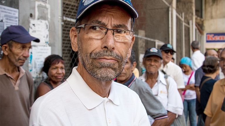 Vanhempi mies lippalakki päässä jonossa Caracasissa, Venezuelassa.