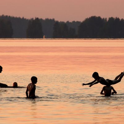 Aikuisia ja lapsia uimassa auringonlaskun aikaan.