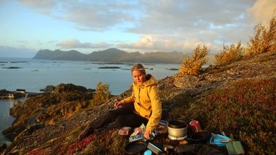 Jonna Salonen istuu kalliolla ympärillään erilaisia ruokatarvikkeita. Taustalla Norjan vuoristoja.