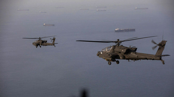 Kaksi sotilashelikopteria lentää meren yllä, alapuolellaan lukuisia tankkerialuksia. (US Central Command / AFP)